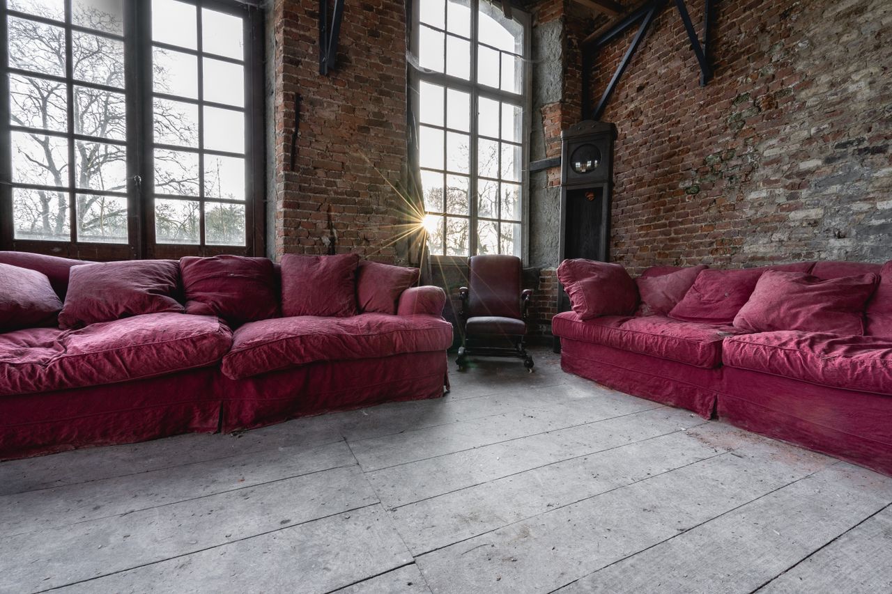 Charming rustic loft interior featuring red velvet sofas, large window panes, and brick walls.