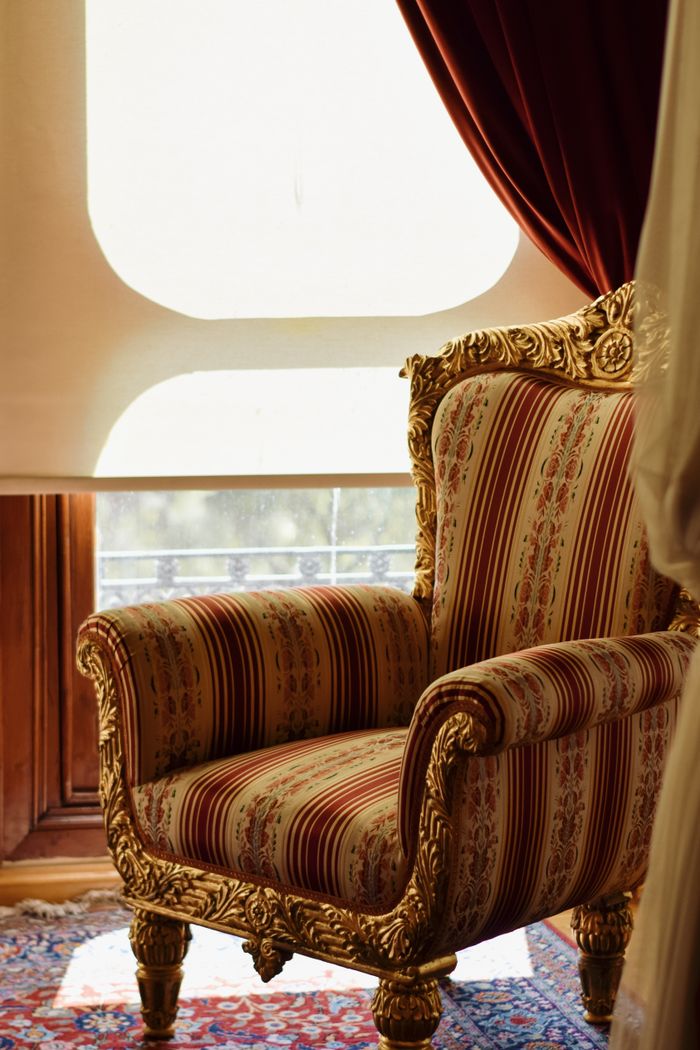 A beautifully decorated vintage armchair sits by a sunlit window, creating a cozy atmosphere.