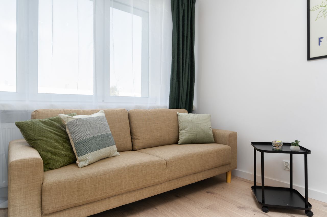 Minimalist living room featuring a beige sofa with green pillows and modern decor.