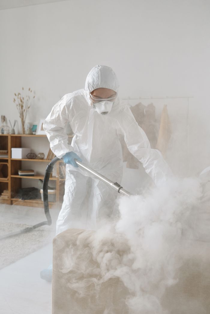Person in a hazmat suit using equipment to disinfect a room, indoors.