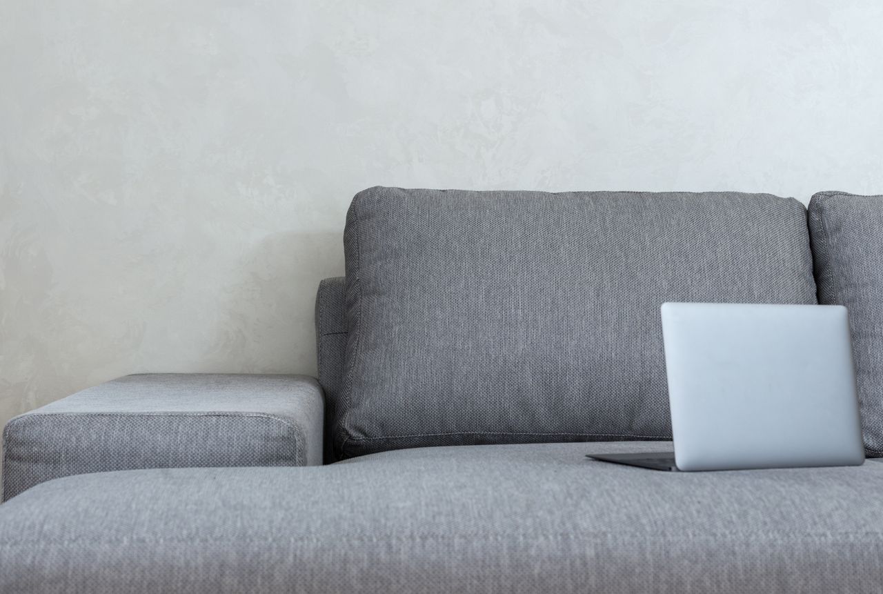 Interior of light modern apartment with open netbook placed on couch with pillows near wall